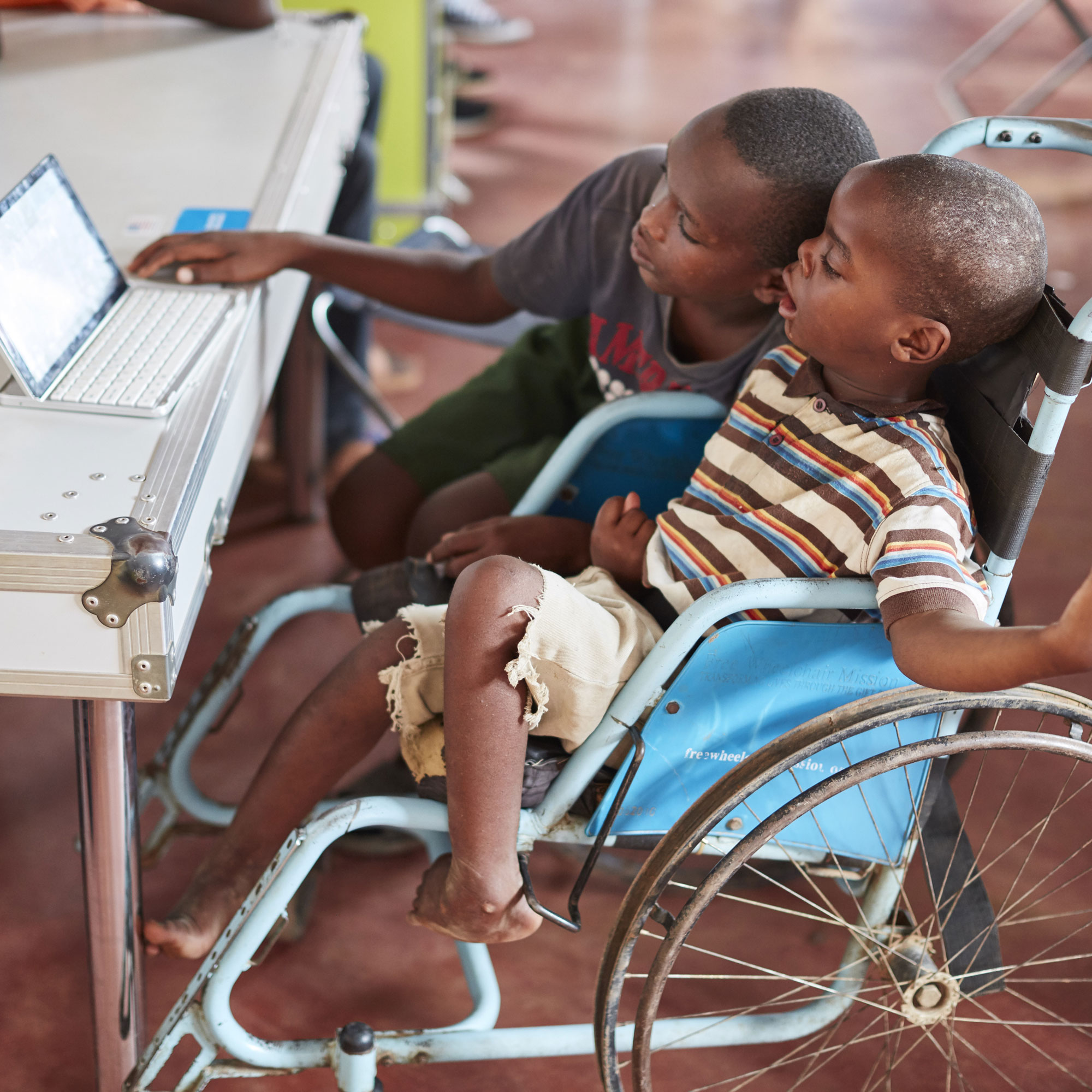 Ruanda: Zwei Kinder in der HI-Ideen-Box. Diese dient als eine Art Jugendzentrum im Mahama-Camp. Das eine Kind zeigt dem anderen Kind im Rollstuhl die Funktionen des Tablets.