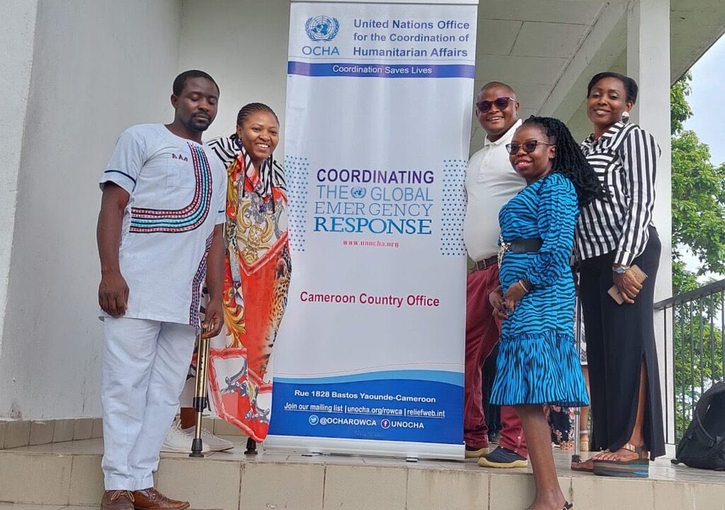 Five workshop participant posing for the photo in front of the UN-OCHA roll-up.