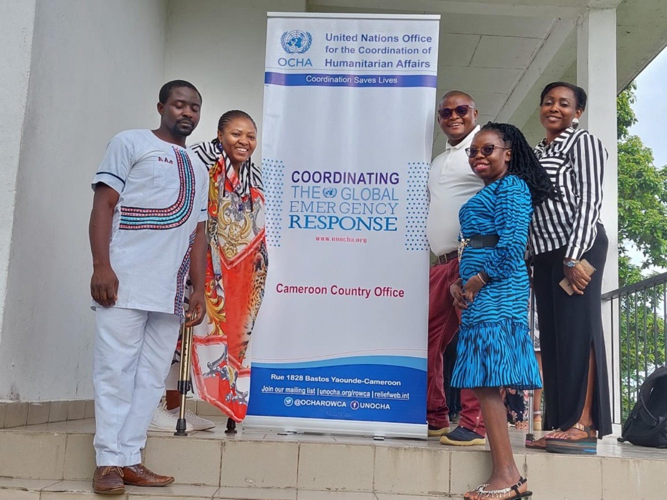 Five workshop participant posing for the photo in front of the UN-OCHA roll-up.