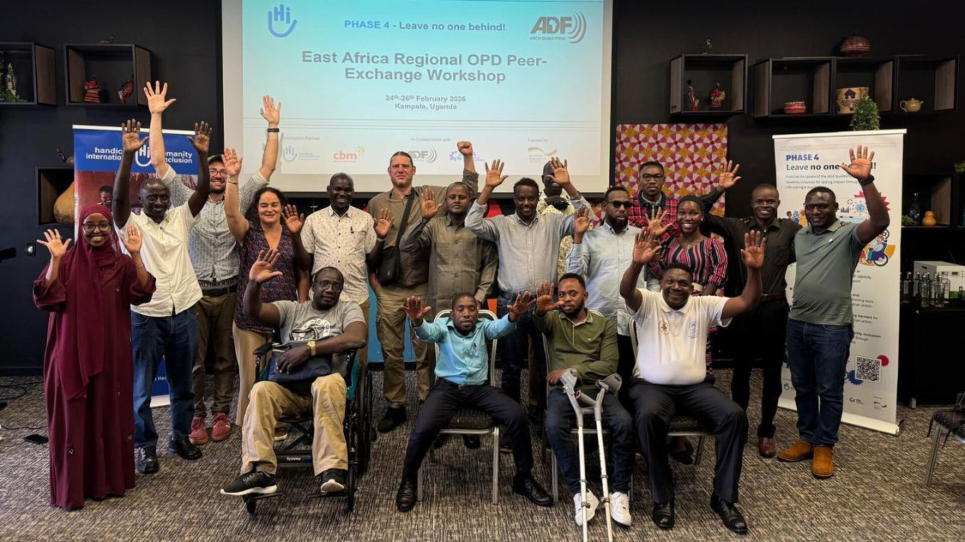 OPD representatives from East Africa laugh and wave in front of a presentation at a peer-exchange event.