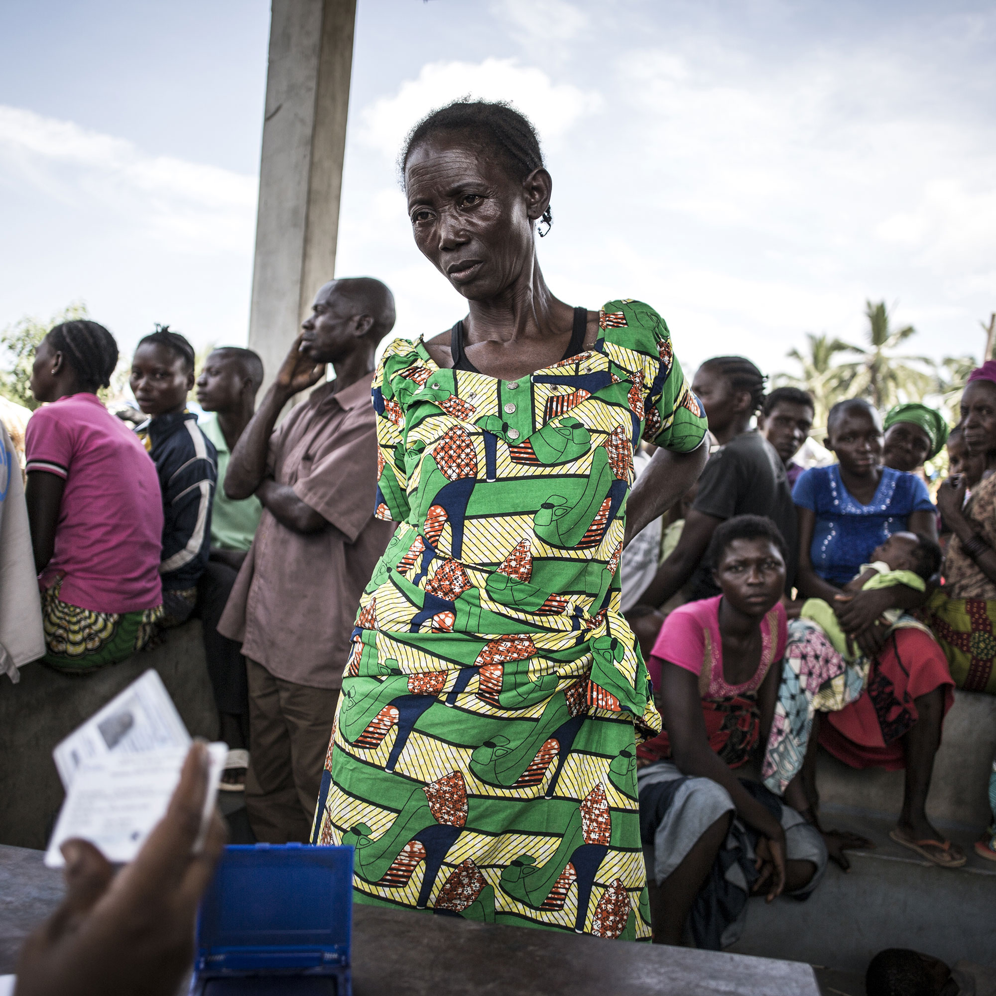 An HI employee checks the identification of a beneficiary. Behind her a queue of other people is waiting.