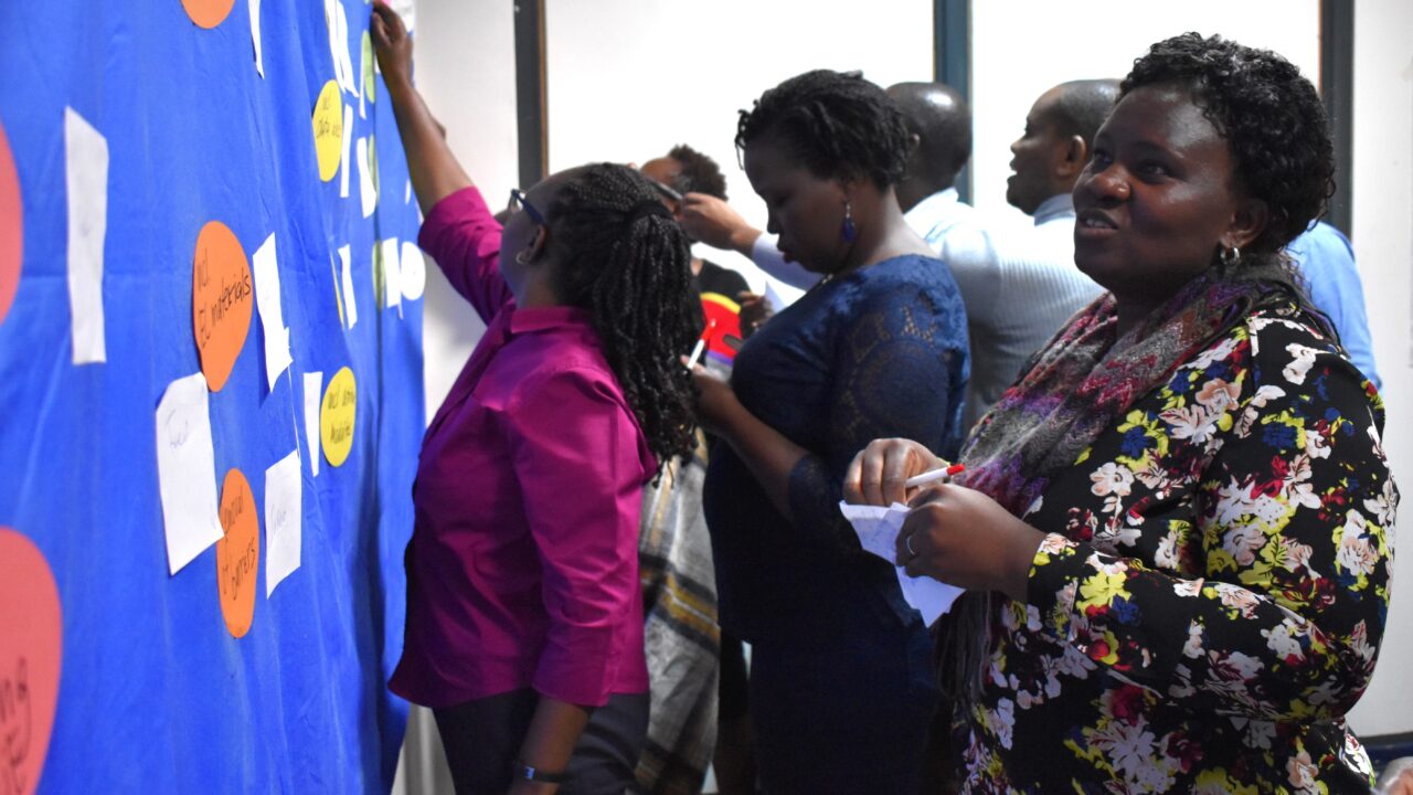 Training participants putting sticky notes to a blue sticky wall.