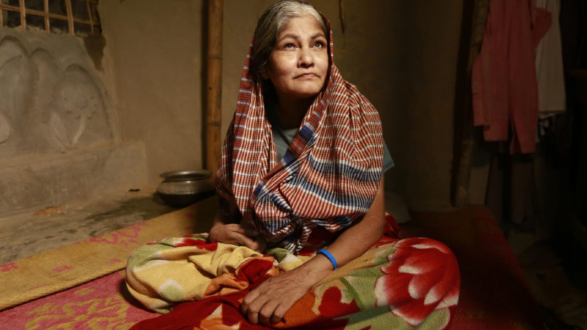 This photo shows an old woman with a physical disability sitting in a house.