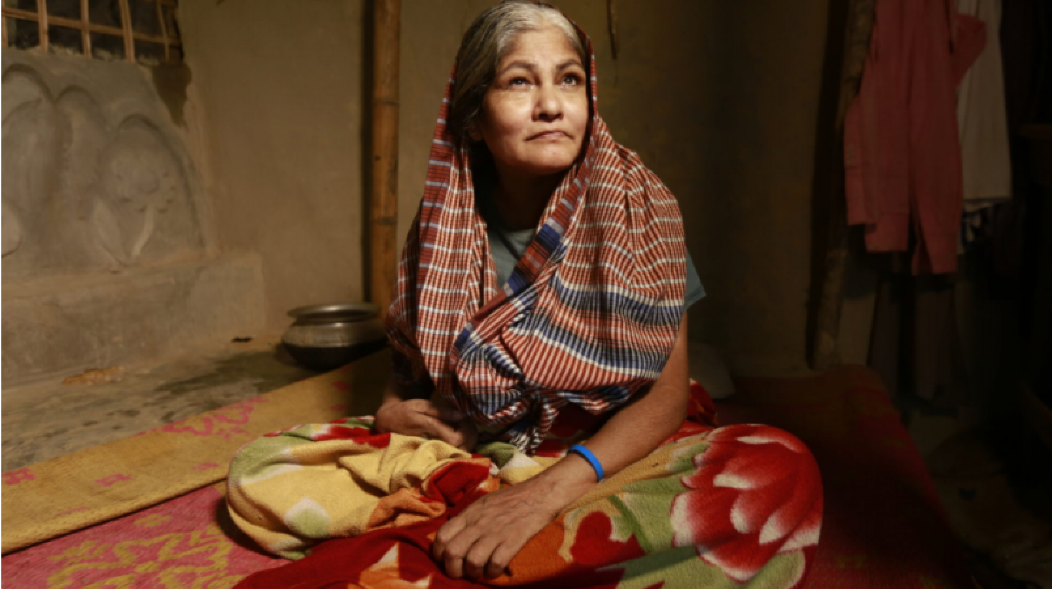 The photo shows an older woman with a physical disability sitting in her house.